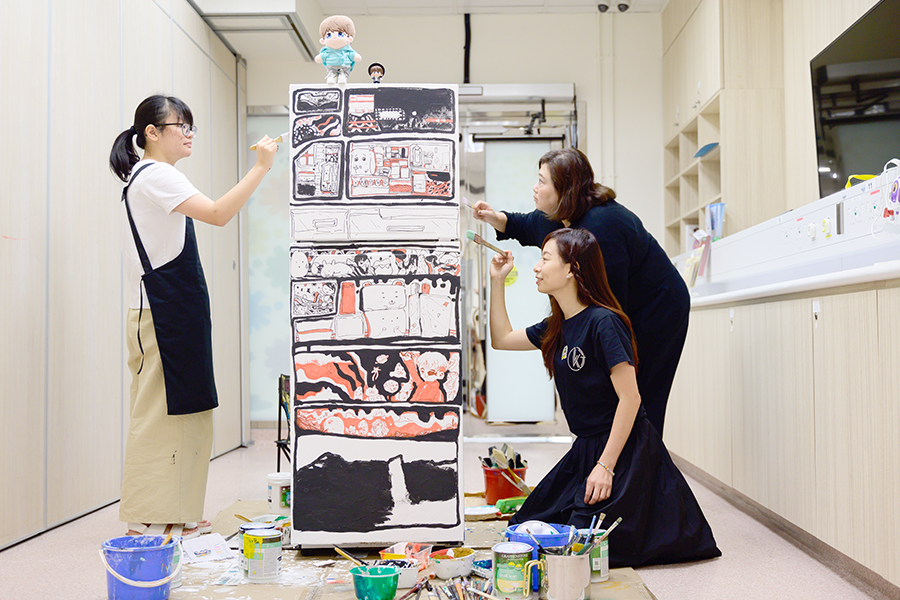 在繪畫冰箱的第五天，（左起）樹仔、Smile和Ellen邊聊天，邊以畫筆修飾畫作線條。