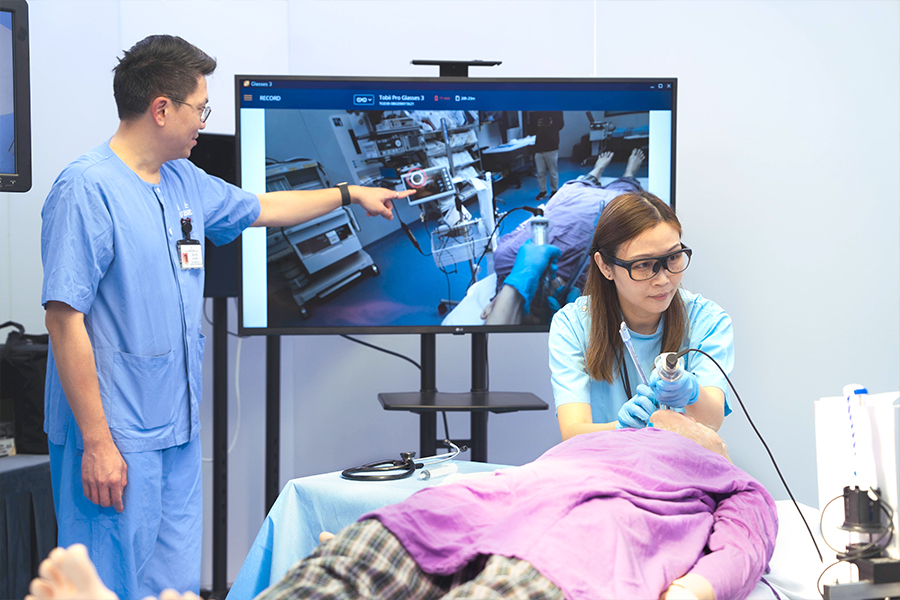 Dr Natalie Leung (right) wears eye-tracking glasses to simulate the intubation process. The visual focus of her gaze is indicated as a red circle on the screen, corresponding to the position pointed out by Tacko Tsoi (left).